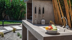 A kitchen counter with a bowl of vegetables, a sink, and hanging kitchen utensils. - Villa Mariani II (Rhodes)