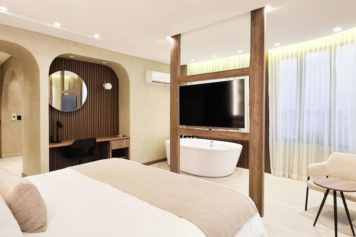 A modern hotel room with a large bed, a TV, a desk, and a chair.