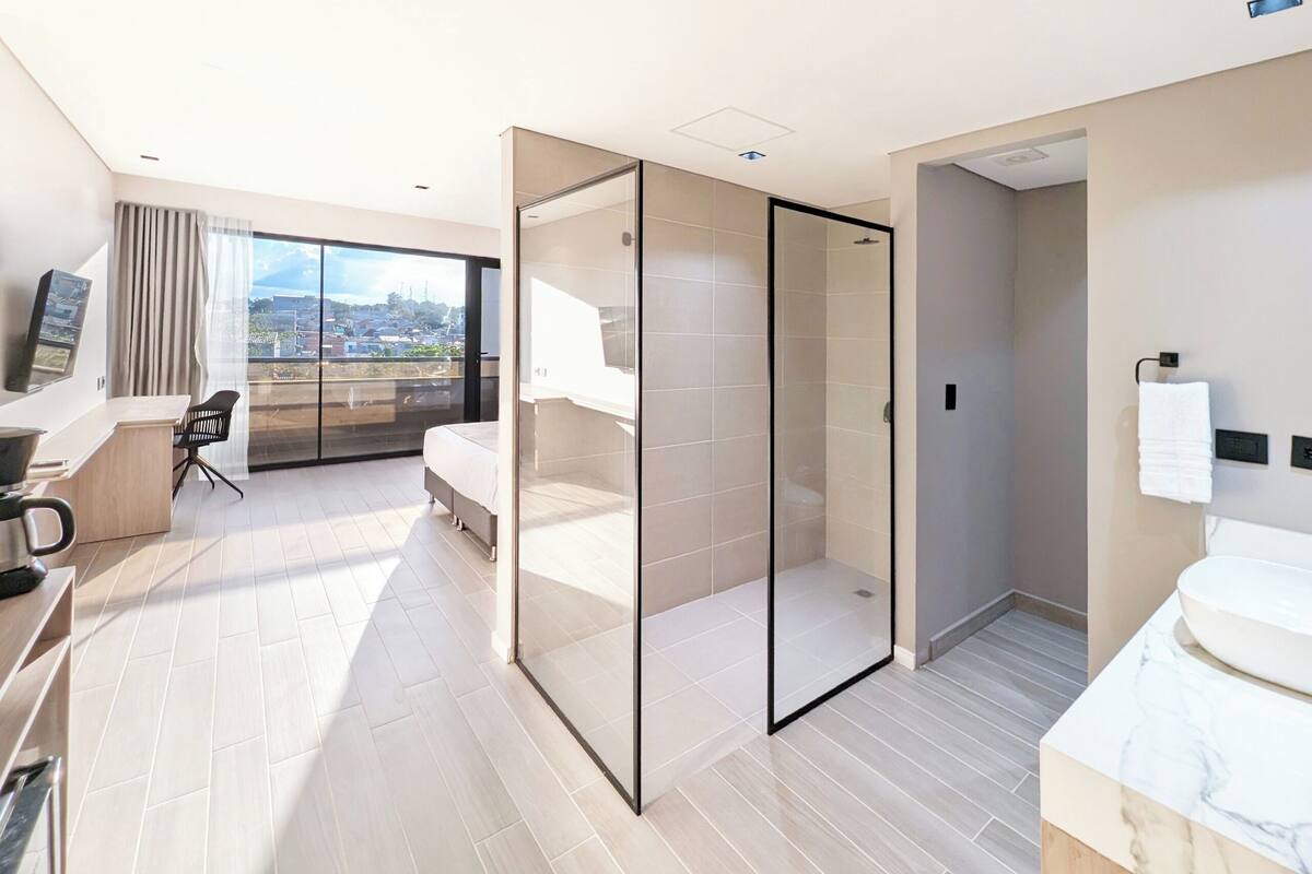 A modern hotel room with a balcony, a shower room, and a desk with a chair.