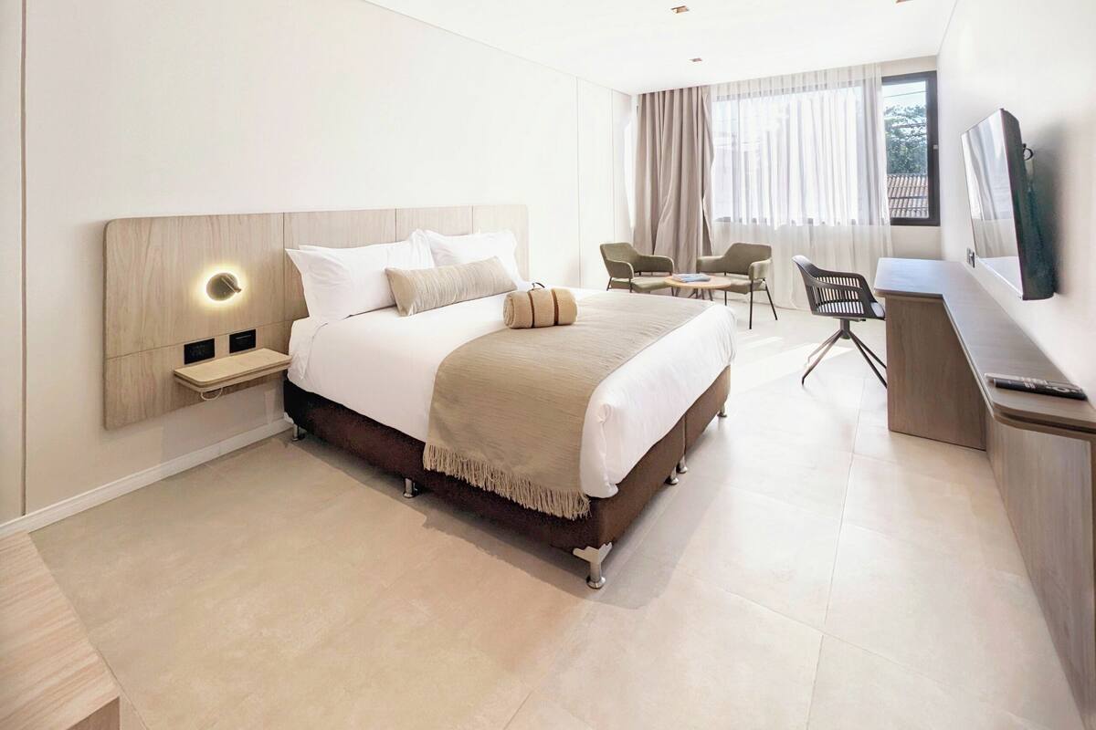 A modern hotel room with a large bed, bedside tables, a desk, and a TV.