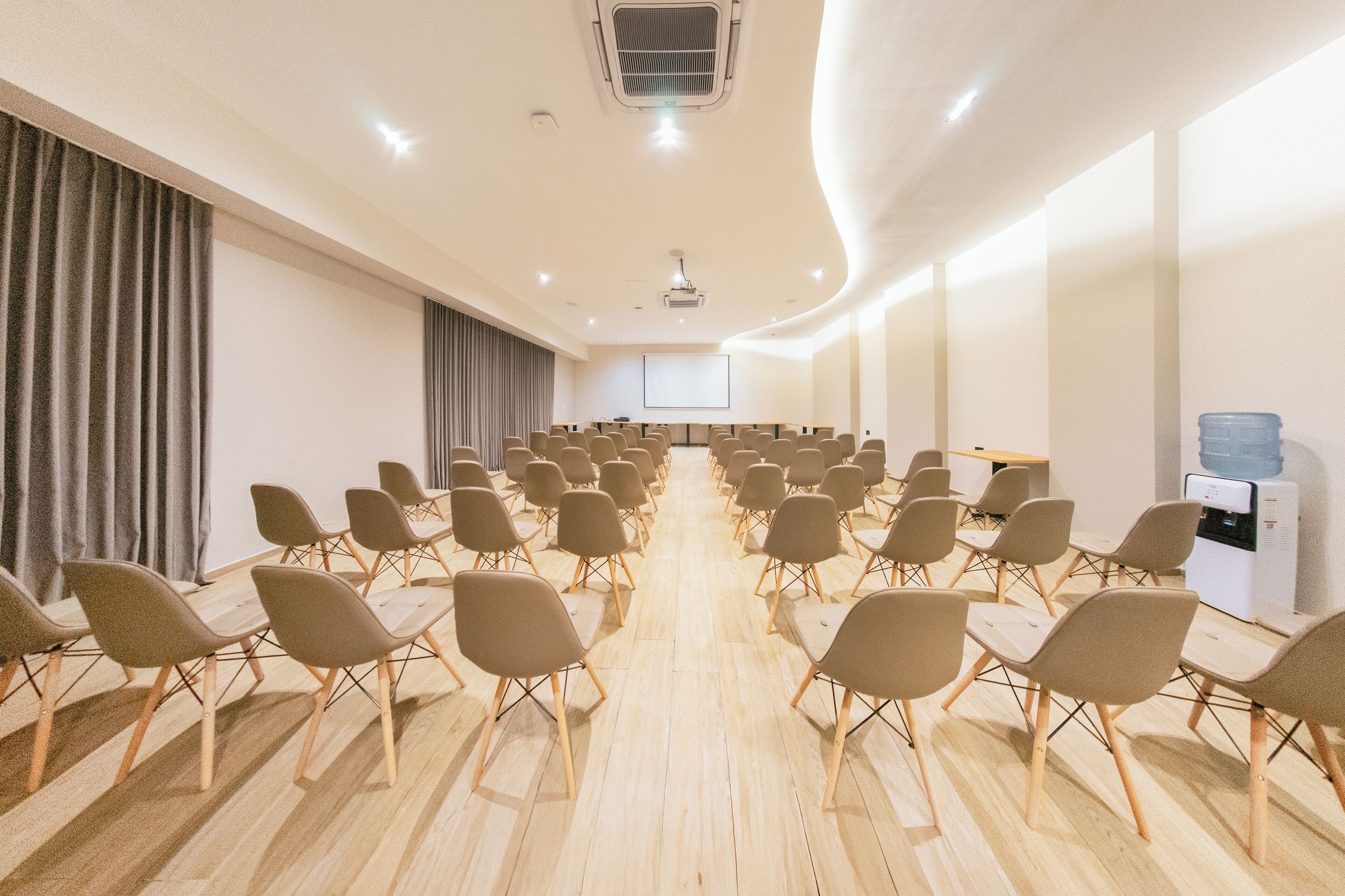 A conference room with rows of chairs, a projector screen, and a water dispenser.