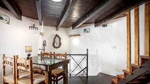 Un comedor con mesa de vidrio, sillas de madera, una araña y una escalera.