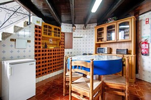 Una cocina con una mesa redonda, sillas de madera, un refrigerador, un microondas y un armario con puertas de vidrio.