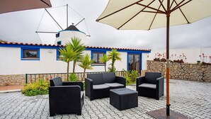 Un patio al aire libre con mobiliario de mimbre, un molino de viento y un muro de piedra.