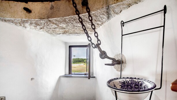 Una habitación con ventana, una cadena metálica colgante y un cuenco con motivos florales.