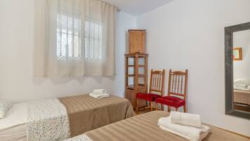A bedroom with two beds, a wooden cabinet, two red chairs, and a mirror on the wall.