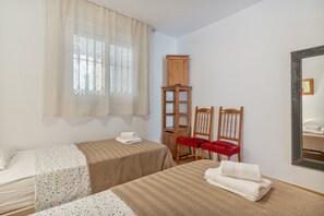 Une chambre avec deux lits, une armoire en bois, deux chaises rouges et un miroir au mur.
