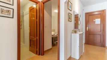 A hallway with wooden doors, a bathroom with a shower, and a bed with a towel.