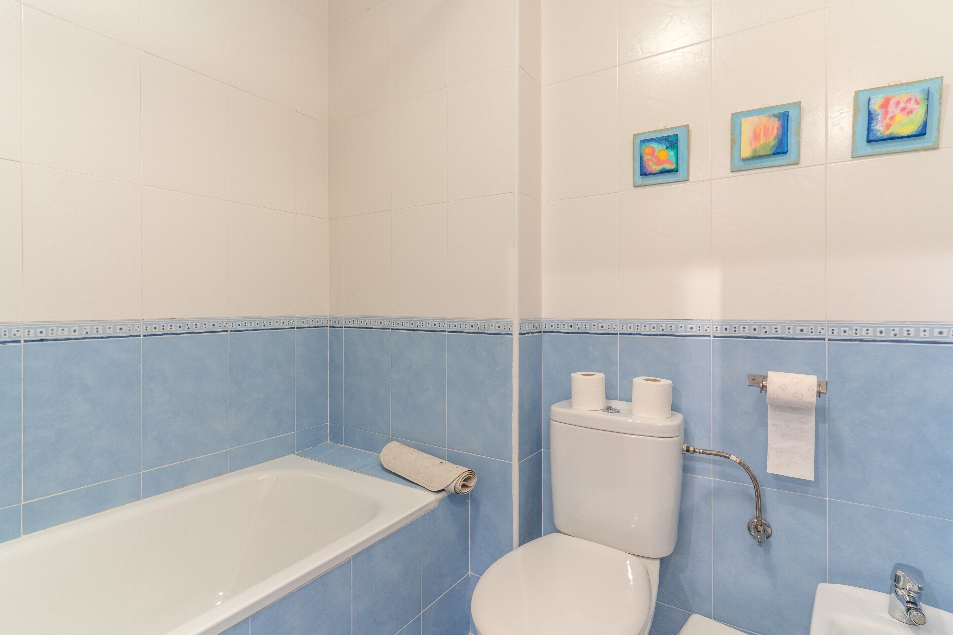 Et badeværelse med badekar, toilet og vask. Tre små kunstværker hænger på væggen.