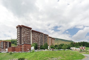 A multi-story hotel with a parking lot in front, surrounded by greenery and hills. - Cosy Villarembert Apartment with Mountain View and Wi-Fi (Villarembert)