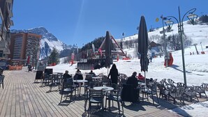 Een houten terras met buitenmeubels, een skilift op de achtergrond en een bergketen.