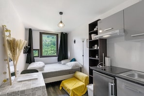 A compact room with a bed, a small kitchenette, a window with a view, and a ceiling light. - Cosy Villarembert Apartment with Mountain View and Wi-Fi (Villarembert)