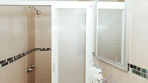 Ein Badezimmer mit beigen Fliesen, einer Dusche mit Duschbrausehandstück und einem Spiegel mit dekorativer Fliesenbordüre.