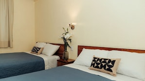 Ein Hotelzimmer mit zwei Betten, jeweils mit blauer Bettdecke und weißen Kissen, einem Nachttisch mit Blumenvase und einer wandmontierten Lampe.