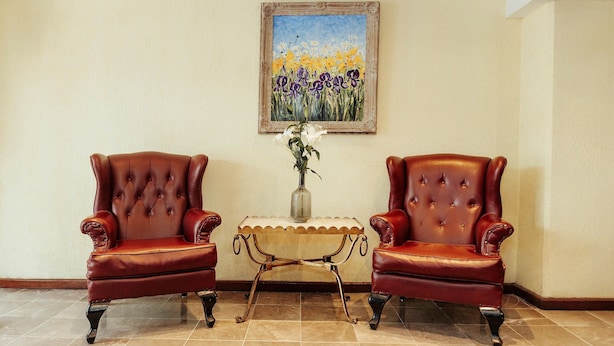 Ein Zimmer mit zwei roten Ledersesseln, einem kleinen Tisch mit einer Vase und einem Blumenbild an der Wand.