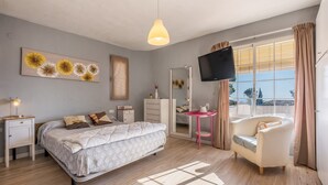 Une chambre à coucher comprenant un lit, des tables de chevet, une coiffeuse, un téléviseur et une fenêtre avec des rideaux.