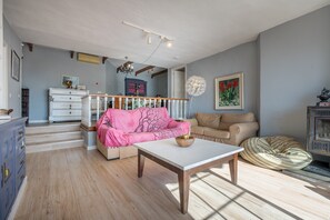A living room with a white table, a pink sofa, a beige sofa, a wooden cabinet, and a patterned bean bag.