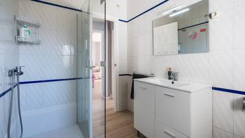 Un baño moderno con cabina de ducha de vidrio, tocador blanco con espejo y perchero.