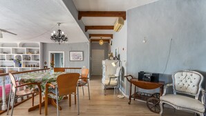Un vaste espace de vie doté d’un plancher en bois, d’un lustre, d’un fauteuil recouvert de tissu blanc et d’une table ancienne.