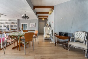 Un vaste espace de vie doté d’un plancher en bois, d’un lustre, d’un fauteuil recouvert de tissu blanc et d’une table ancienne.