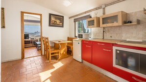 Cocina compacta con gabinetes rojos, lavavajillas y microondas. Hay un comedor con mesa y sillas de madera.