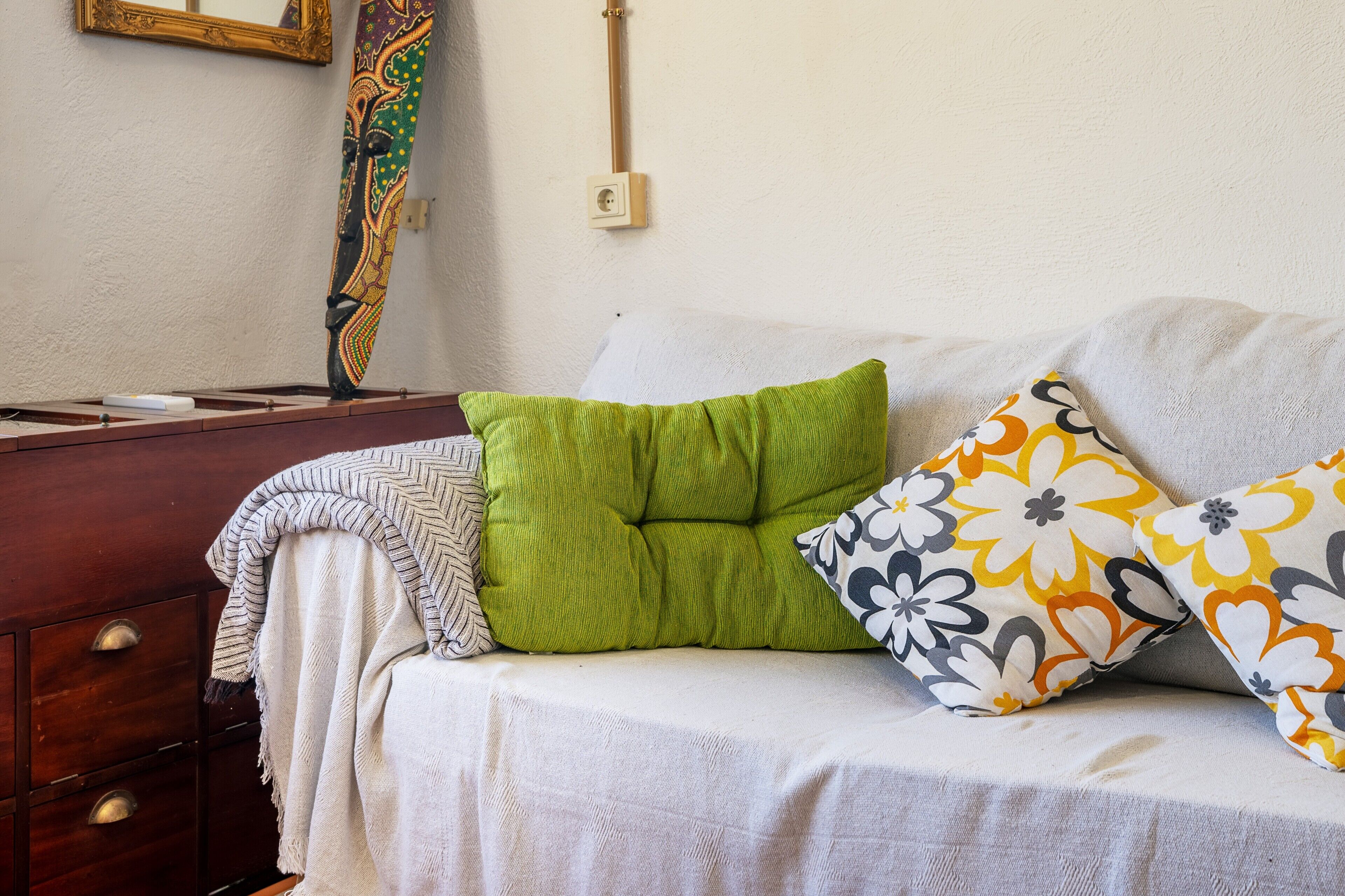 Een bank met gekleurde kussens, een houten dressoir en een decoratief object aan de muur.