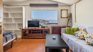 Una sala de estar con un sofá, un televisor, un mueble de madera, una mesa y un ventanal con vistas.