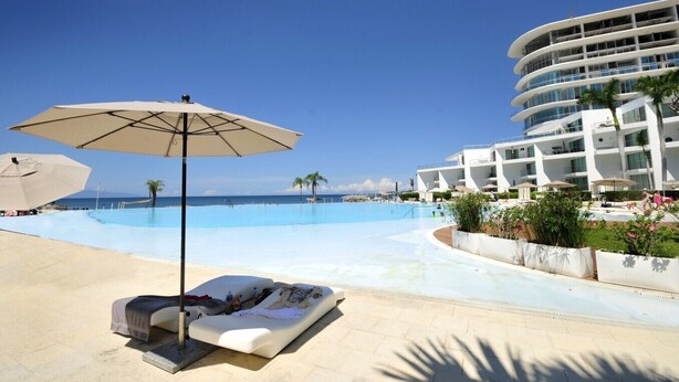 A pool area with a lounge chair and umbrella, a large building with balconies, and a clear blue sky. - Beachfront condo in the heart of Nuevo Vallarta (Nuevo Vallarta)