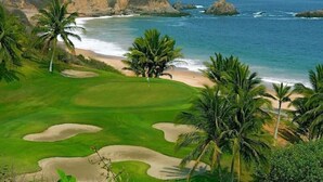 A golf course with a beach view, palm trees, and a mountainous backdrop. - Beachfront condo in the heart of Nuevo Vallarta (Nuevo Vallarta)
