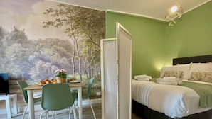 Une pièce comprenant un lit, une table à manger avec des chaises et une fresque représentant des arbres sur le mur.