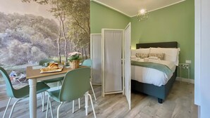 Une pièce comprenant un lit, une table à manger avec des chaises, une fresque murale et un luminaire suspendu.