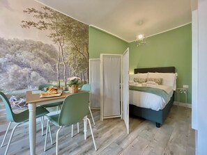 Una stanza con un letto, un tavolo da pranzo con sedie, un affresco a parete e una lampada a sospensione.