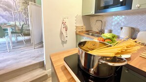 Une cuisine équipée d’une cuisinière, d’un évier et d’un four à micro-ondes. Une casserole contenant des pâtes et des légumes est posée sur la cuisinière.