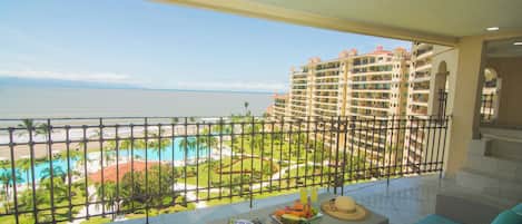 A balcony with a view of a resort pool, palm trees, and a beach.
