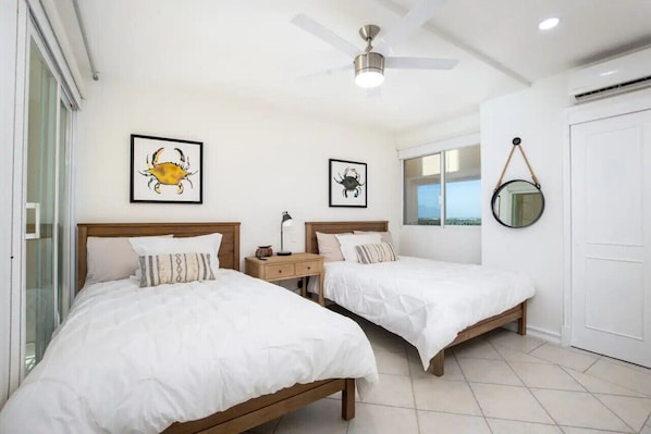 Une chambre avec deux lits, un ventilateur de plafond et des œuvres d’art encadrées accrochées aux murs.