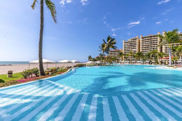 Zwembad van een resort met helderblauw water, omgeven door palmbomen en ligbedden.