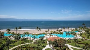 Un complexe hôtelier doté d’une grande piscine, de palmiers et offrant une vue sur la plage.