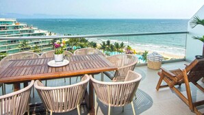 A wooden table with wicker chairs, a potted plant, and a view of the ocean and beach.
