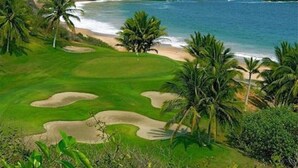 A golf course with sand bunkers, palm trees, and a beach view.