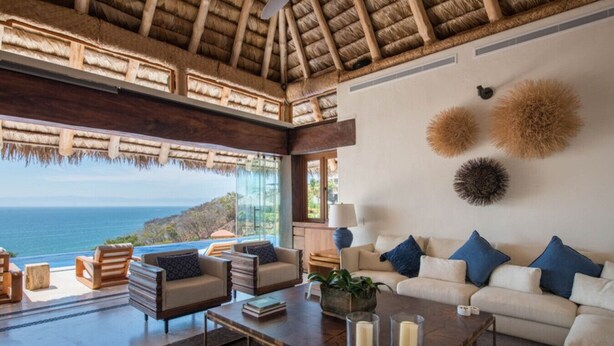 A spacious living room with a large window overlooking the ocean, a high ceiling with a thatched roof, and a comfortable seating area with a sofa and chairs. - Luxury staffed villa chef included-Punta Mita Corridor (La Cruz de Huanacaxtle)