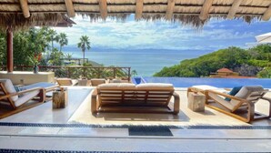 A poolside area with lounge chairs and a thatched roof, overlooking a body of water and greenery. - Luxury staffed villa chef included-Punta Mita Corridor (La Cruz de Huanacaxtle)