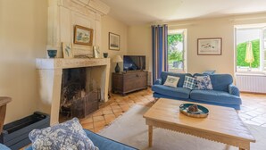 A living room with a fireplace, a blue sofa, a wooden coffee table, and a view of the outdoors through large windows. - Holiday Home 'Maison De Vacances Avec Piscine' with Private Pool, Private Terrace and Wi-Fi (Sainte-Gemme)
