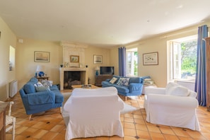 A living room with a fireplace, blue sofas, white armchairs, and a television. - Holiday Home 'Maison De Vacances Avec Piscine' with Private Pool, Private Terrace and Wi-Fi (Sainte-Gemme)