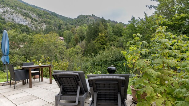 An outdoor patio with two chairs, a table, and a blue umbrella. - La Sabaudia En Chartreuse Apartment with Mountain View, Private Terrace, and Wi-Fi (Saint-Pierre-d'Entremont)
