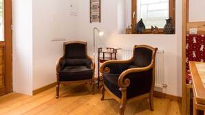 A room with two wooden armchairs, a small table, a floor lamp, a radiator, and a window with a red patterned curtain. - La Sabaudia En Chartreuse Apartment with Mountain View, Private Terrace, and Wi-Fi (Saint-Pierre-d'Entremont)