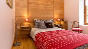 A bedroom with a wooden headboard, two bedside tables with lamps, a red patterned bedspread, and a chair with a red cushion. - La Sabaudia En Chartreuse Apartment with Mountain View, Private Terrace, and Wi-Fi (Saint-Pierre-d'Entremont)