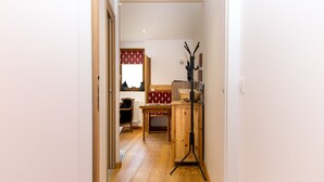 A narrow hallway with wooden flooring, a wooden cabinet with a black stand, and a red patterned tablecloth. - La Sabaudia En Chartreuse Apartment with Mountain View, Private Terrace, and Wi-Fi (Saint-Pierre-d'Entremont)