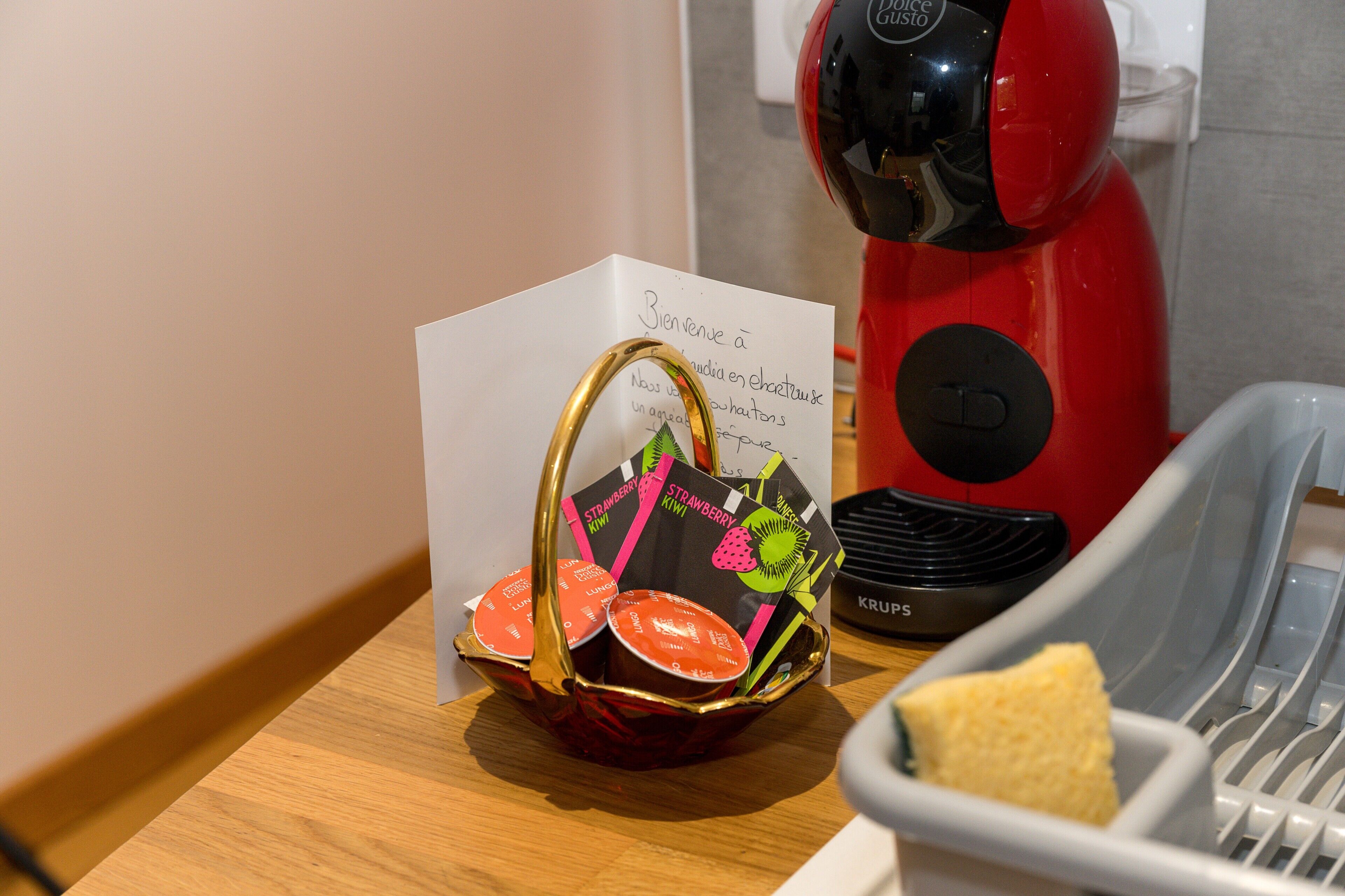 Eine Küchenzeile mit einer roten Kaffeemaschine, einem Korb voller Essbehälter und einer Notiz auf der Arbeitsfläche.