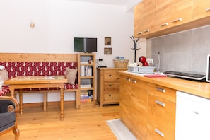Cocina compacta con armarios de madera, televisor integrado y zona de comedor con banco.