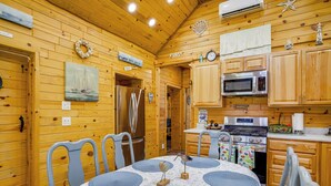A cozy wooden cabin interior with a dining table, chairs, a refrigerator, a microwave, and a stove.
